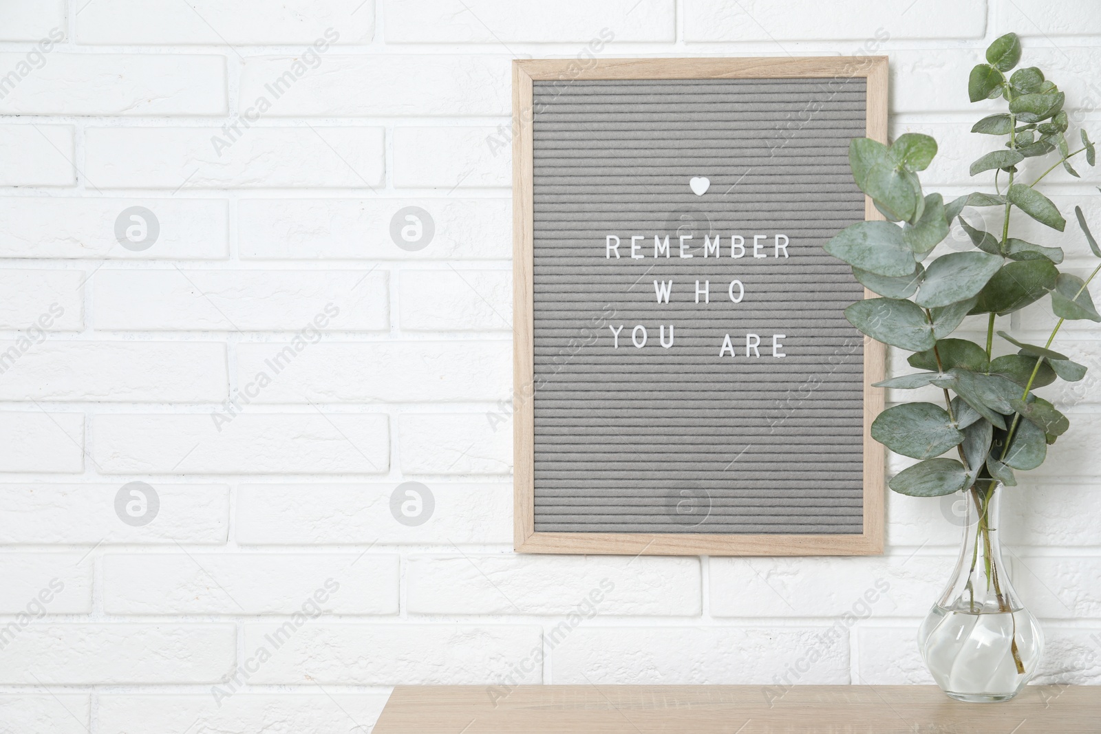 Photo of Letter board with phrase Remember Who You Are and eucalyptus branches in vase on wooden table indoors, space for text