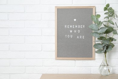 Letter board with phrase Remember Who You Are and eucalyptus branches in vase on wooden table indoors, space for text