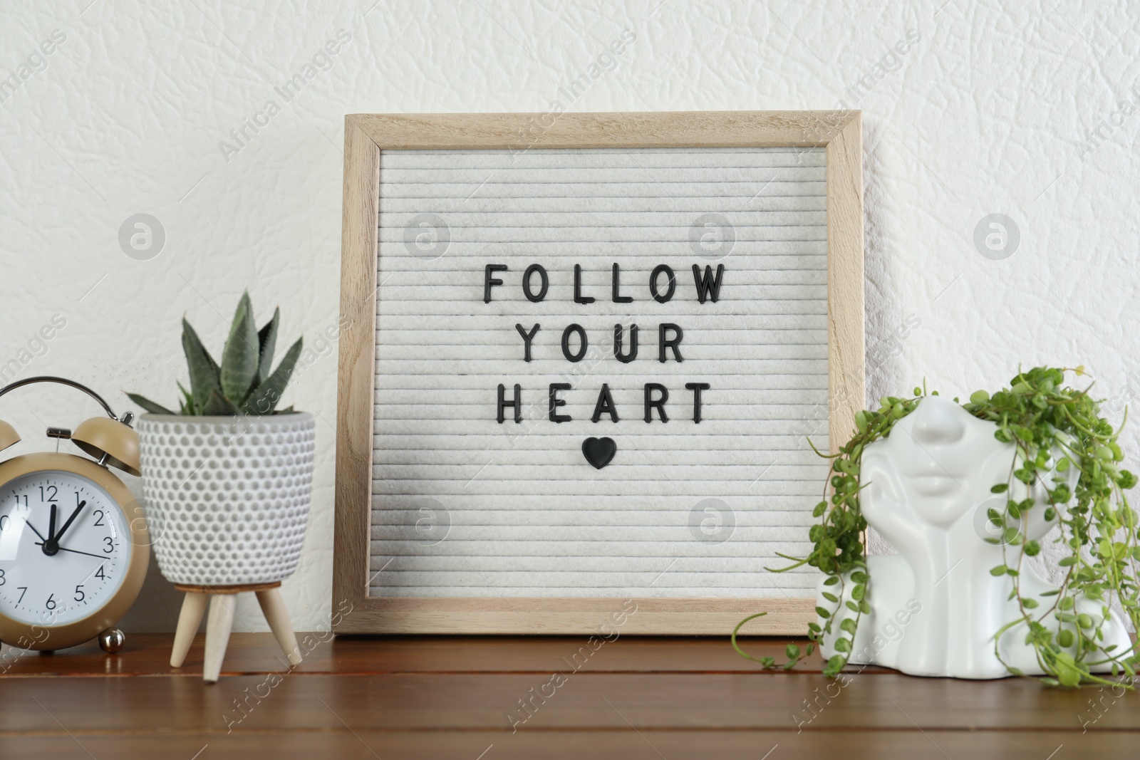 Photo of Letter board with phrase Follow Your Heart, alarm clock and plants on wooden table