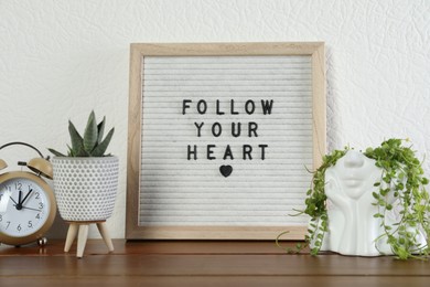 Letter board with phrase Follow Your Heart, alarm clock and plants on wooden table