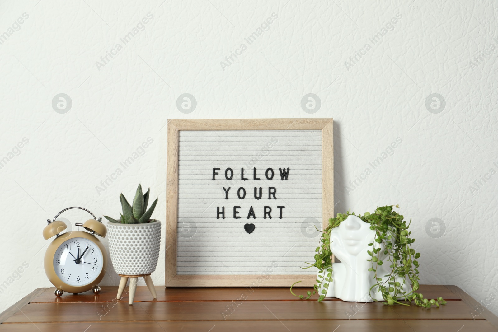 Photo of Letter board with phrase Follow Your Heart, alarm clock and plants on wooden table