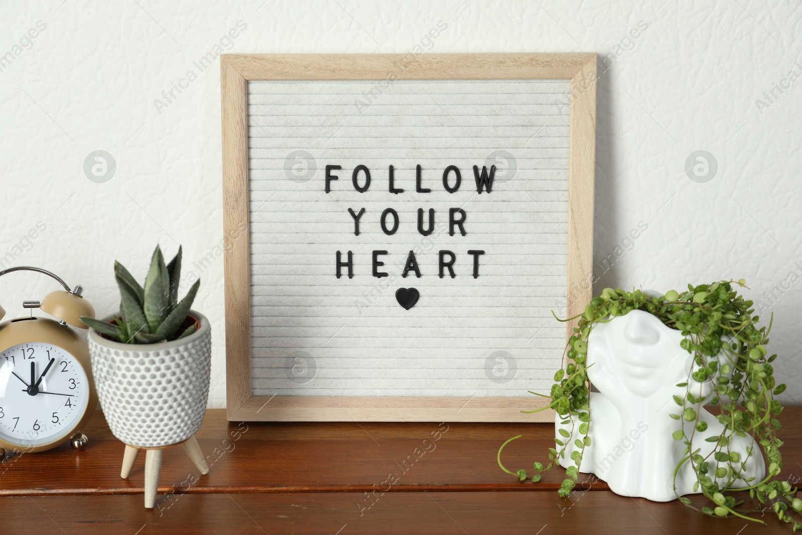 Photo of Letter board with phrase Follow Your Heart, alarm clock and plants on wooden table