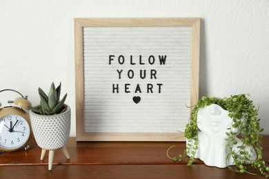 Photo of Letter board with phrase Follow Your Heart, alarm clock and plants on wooden table