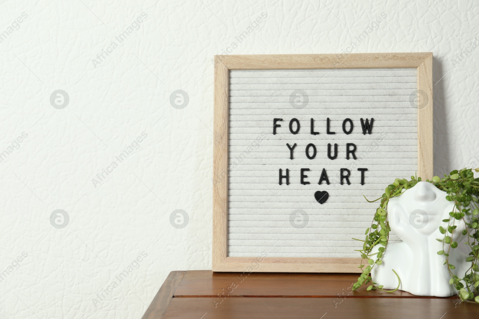 Photo of Letter board with phrase Follow Your Heart and plant on wooden table, space for text