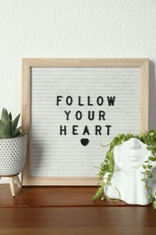 Letter board with phrase Follow Your Heart and plants on wooden table