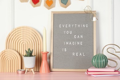 Photo of Letter board with phrase Everything You Can Imagine Is Real and decor elements on pink wooden table