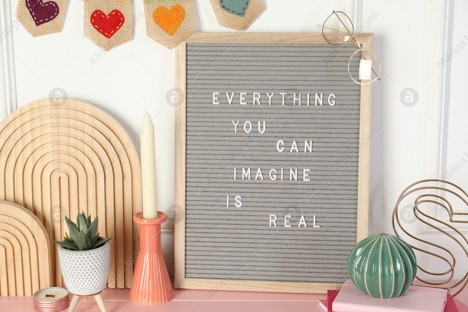 Photo of Letter board with phrase Everything You Can Imagine Is Real and decor elements on pink wooden table