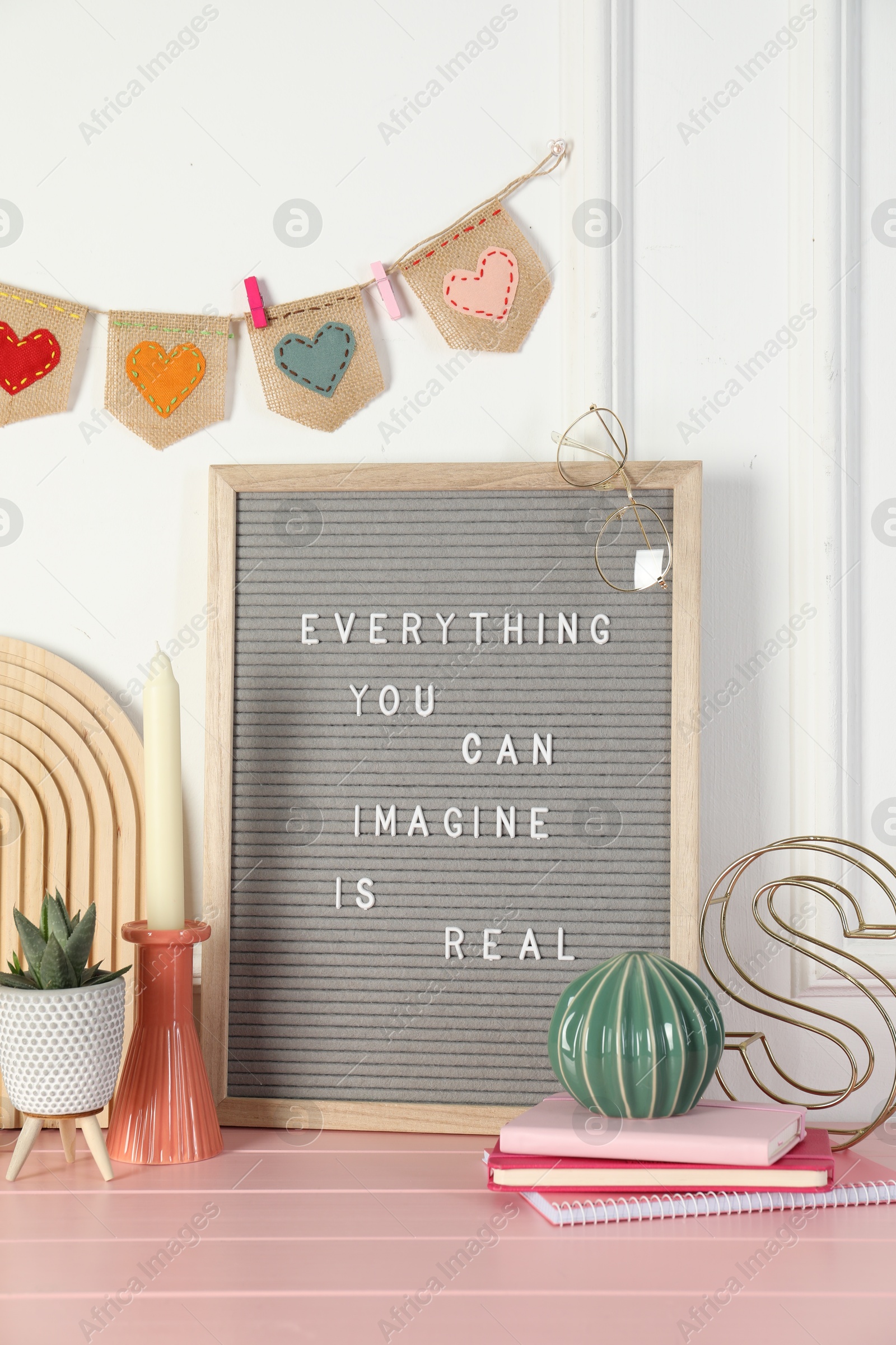 Photo of Letter board with phrase Everything You Can Imagine Is Real and decor elements on pink wooden table