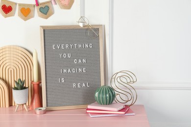 Letter board with phrase Everything You Can Imagine Is Real and decor elements on pink wooden table. Space for text