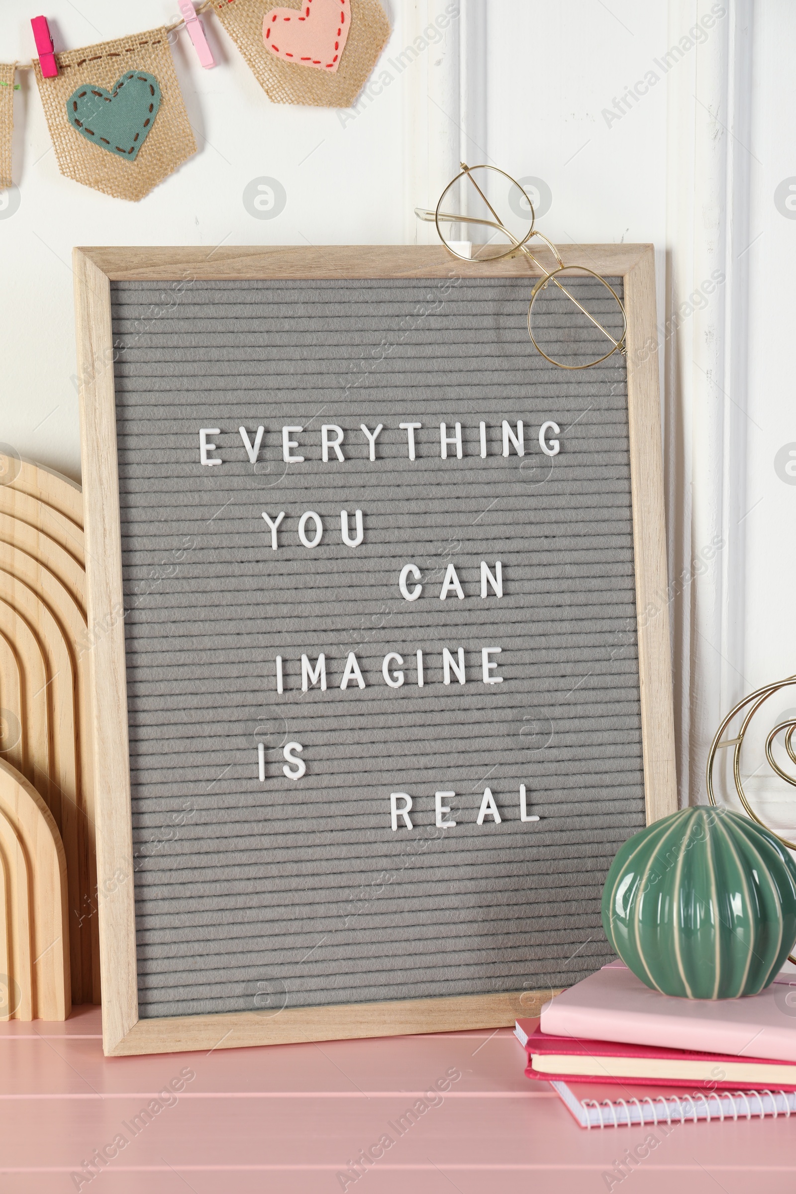 Photo of Letter board with phrase Everything You Can Imagine Is Real and decor elements on pink wooden table