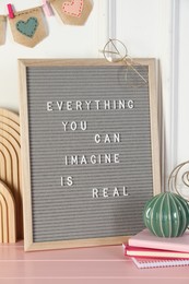 Letter board with phrase Everything You Can Imagine Is Real and decor elements on pink wooden table