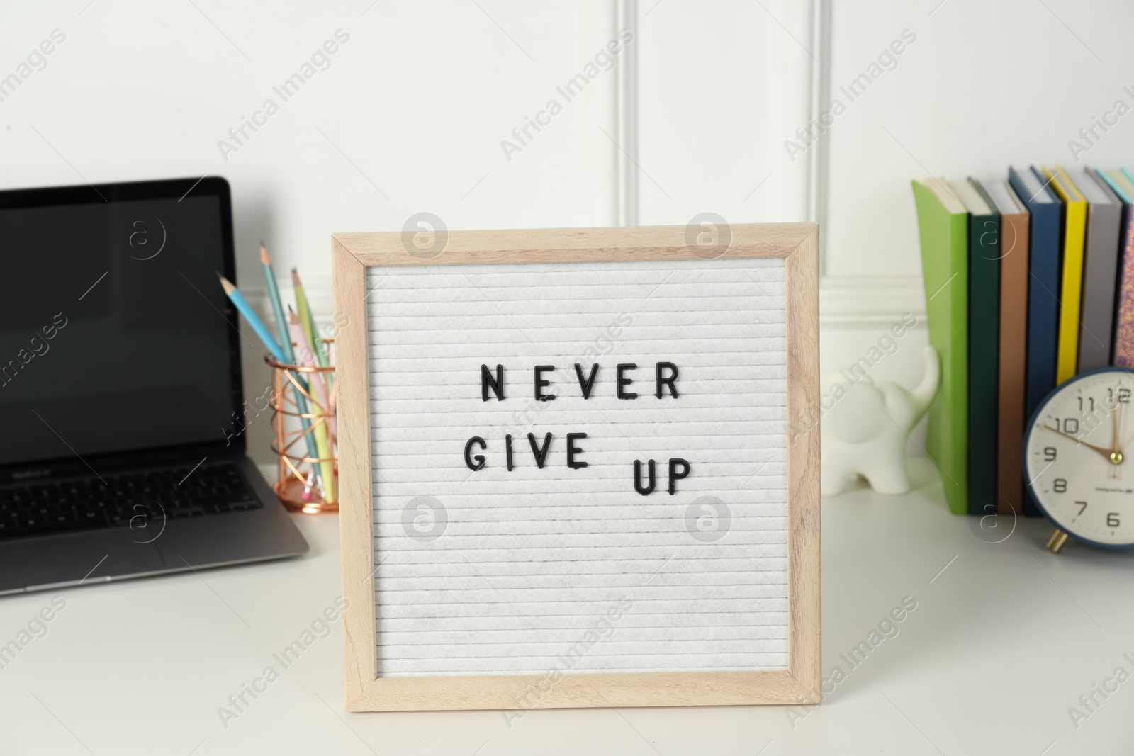 Photo of Letter board with phrase Never Give Up, laptop, alarm clock and stationery on white desk