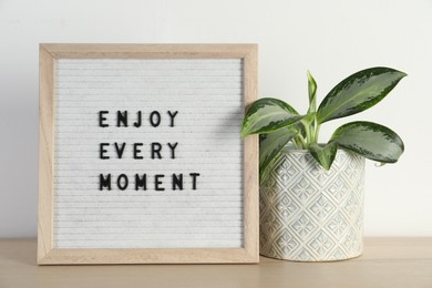 Letter board with phrase Enjoy Every Moment and plant on wooden table