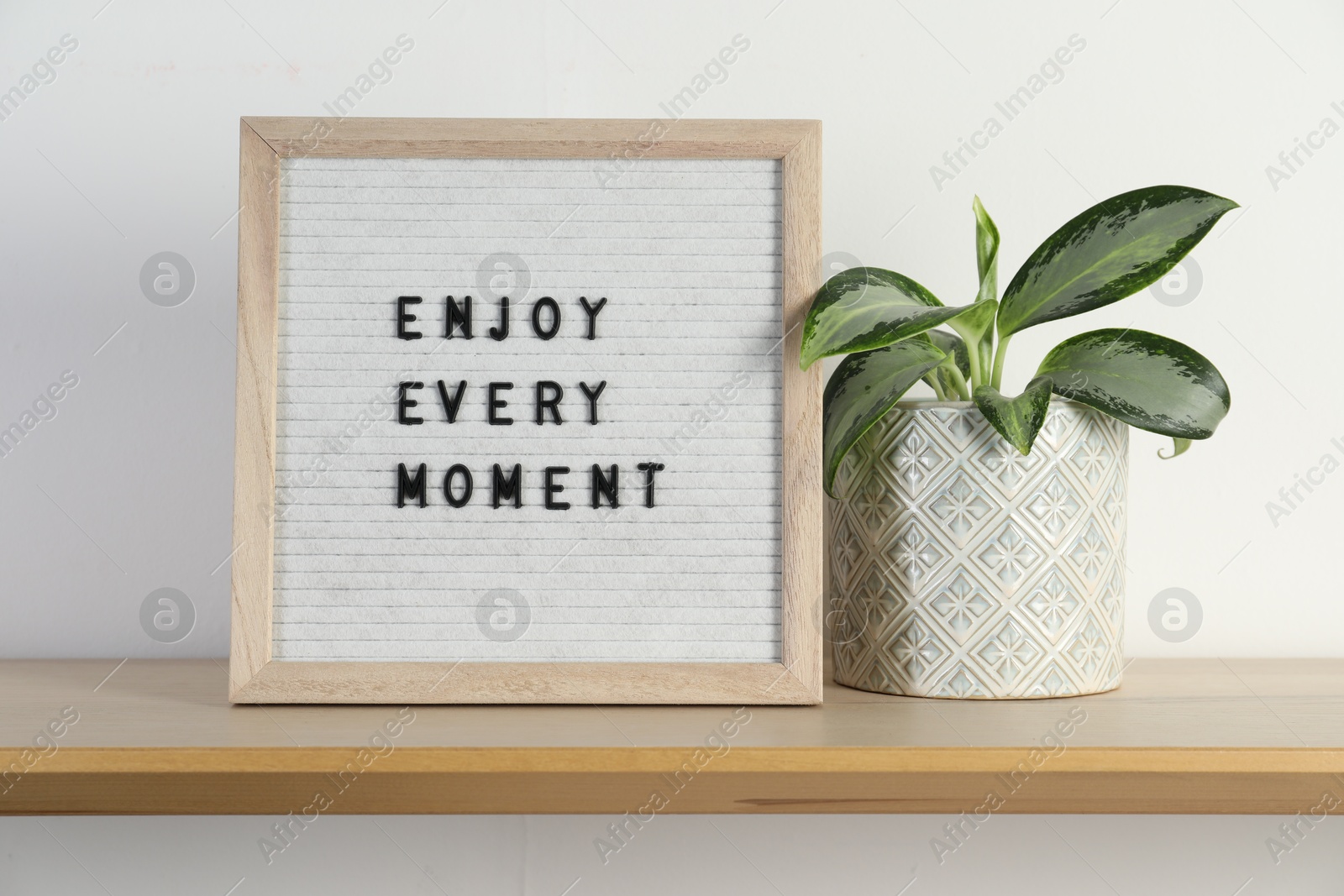 Photo of Letter board with phrase Enjoy Every Moment and plant on wooden table