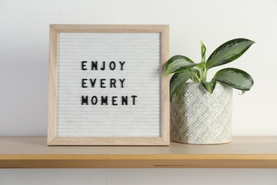 Letter board with phrase Enjoy Every Moment and plant on wooden table