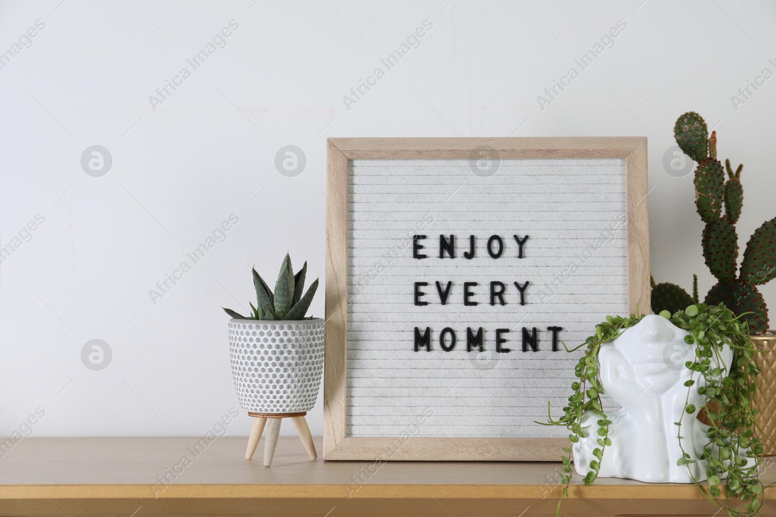 Photo of Letter board with phrase Enjoy Every Moment and plants on wooden table. Space for text