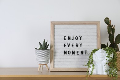 Letter board with phrase Enjoy Every Moment and plants on wooden table. Space for text