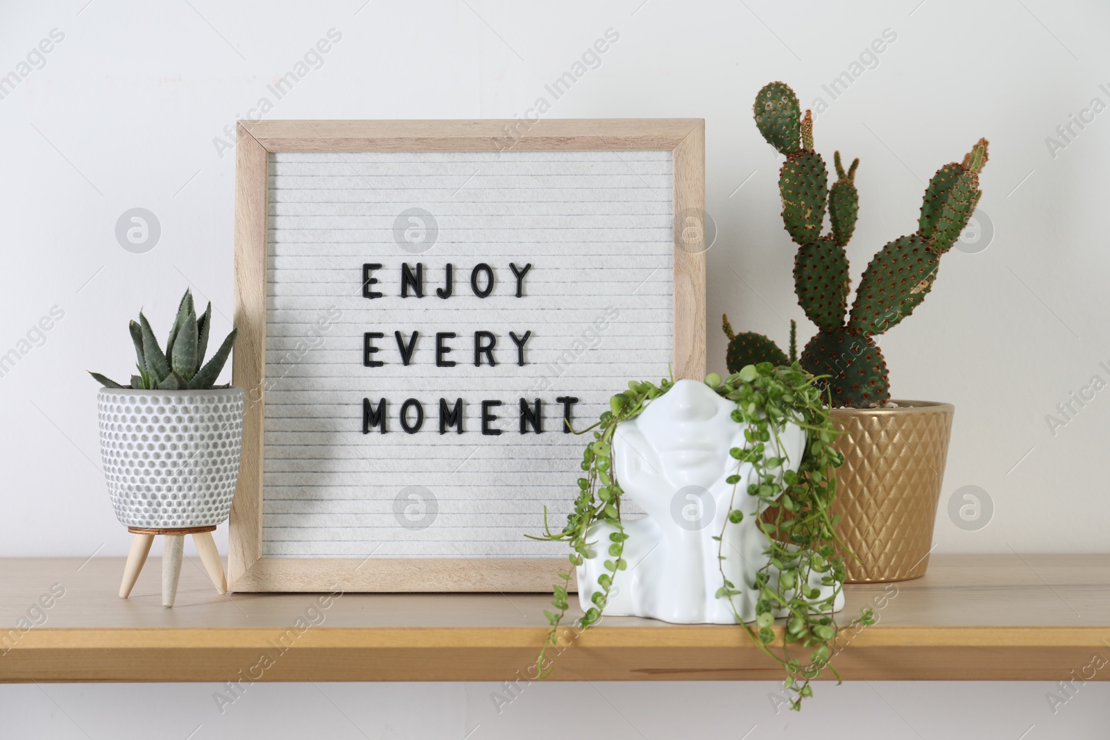 Photo of Letter board with phrase Enjoy Every Moment and plants on wooden table