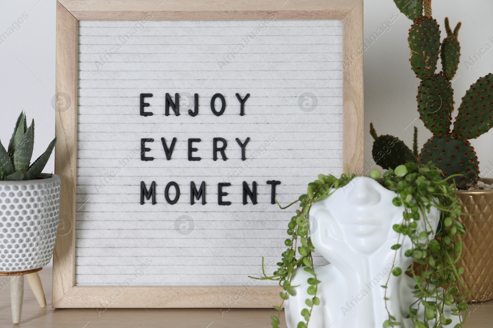 Photo of Letter board with phrase Enjoy Every Moment and plants on wooden table