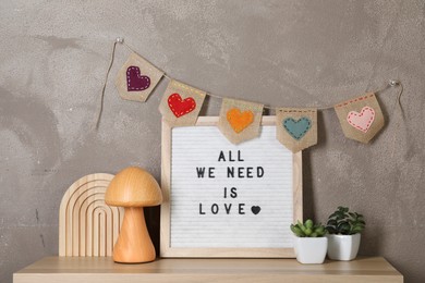 Letter board with phrase All We Need Is Love, plants and decor elements on wooden table