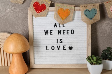 Letter board with phrase All We Need Is Love, plants and decor elements on wooden table