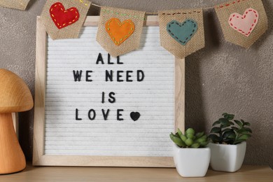 Letter board with phrase All We Need Is Love, plants and decor elements on wooden table