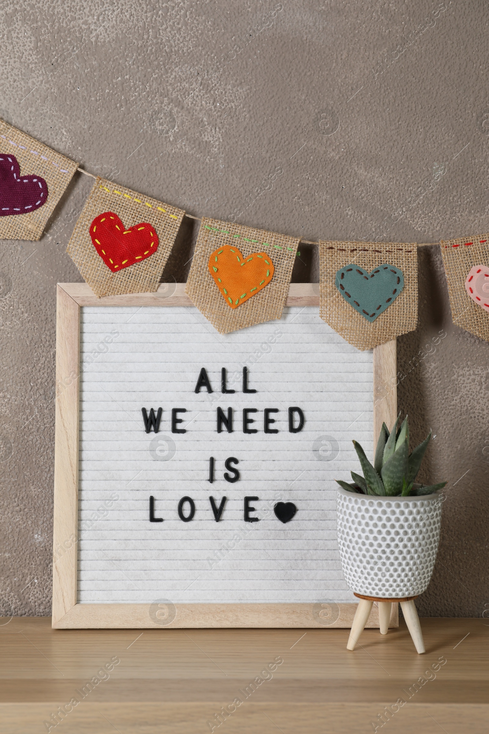 Photo of Letter board with phrase All We Need Is Love and plant on wooden table