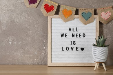 Letter board with phrase All We Need Is Love and plant on wooden table. Space for text