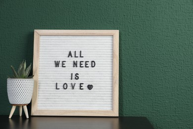 Photo of Letter board with phrase All We Need Is Love and plant on table near green wall. Space for text