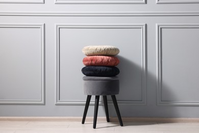 Photo of Stylish stool and cushions near light grey wall indoors