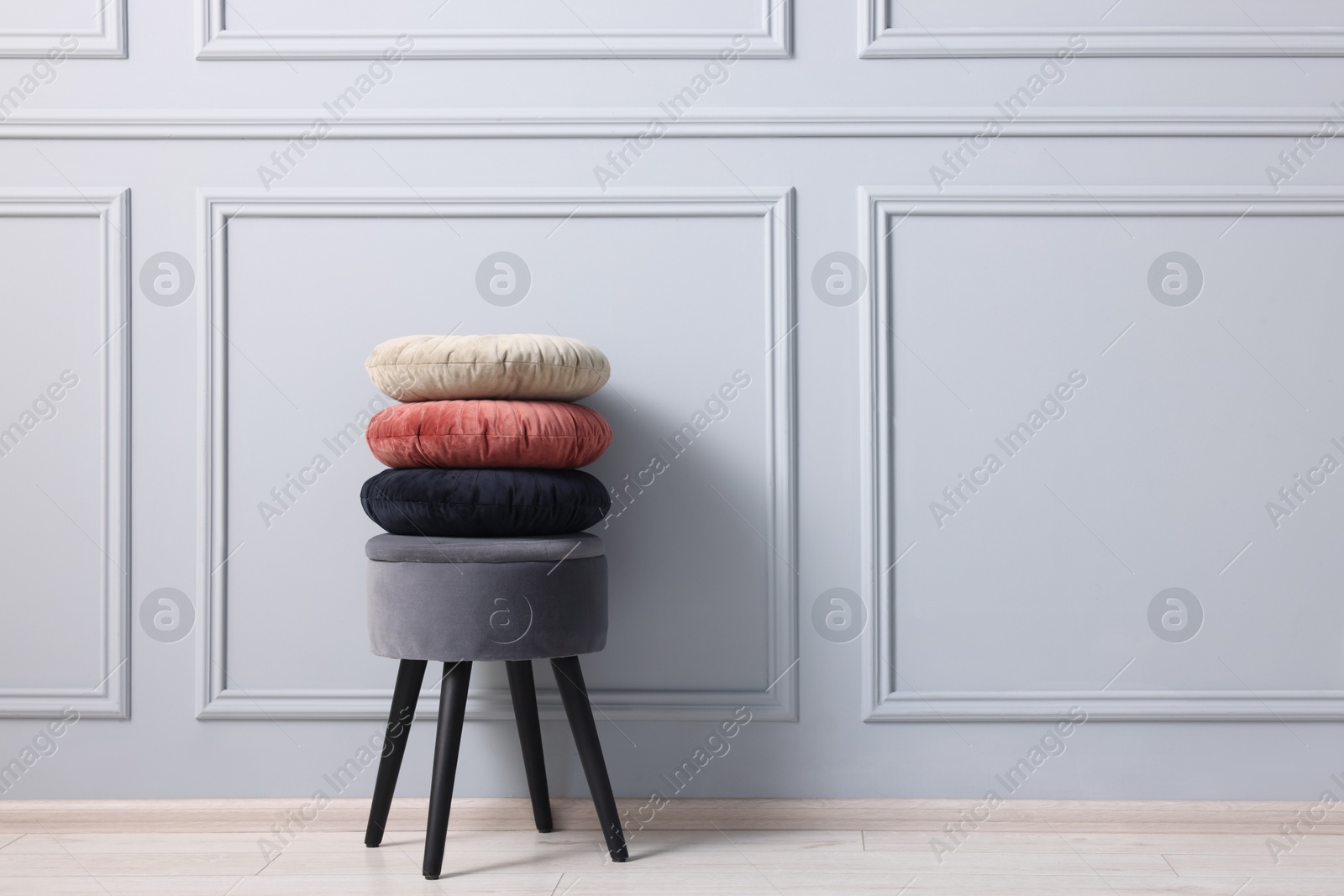 Photo of Stylish stool and cushions near light grey wall indoors, space for text