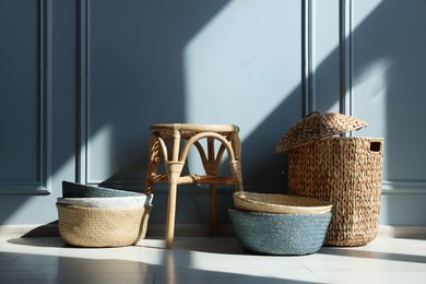 Photo of Stylish stool and many wicker baskets near light grey wall indoors