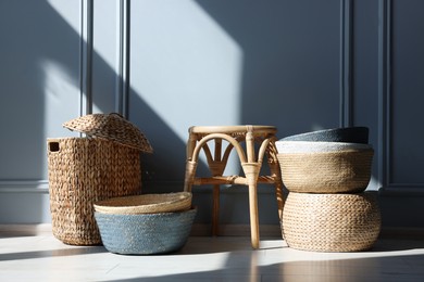 Photo of Stylish stool and many wicker baskets near light grey wall indoors