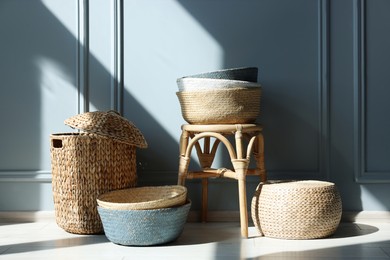 Photo of Stylish stool and many wicker baskets near light grey wall indoors