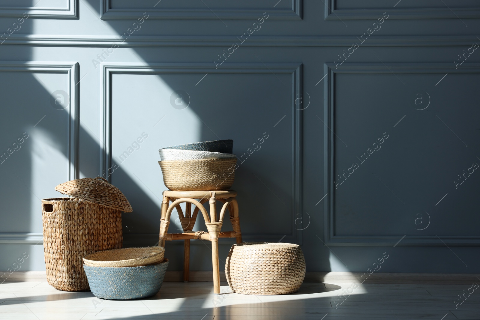 Photo of Stylish stool and many wicker baskets near light grey wall indoors