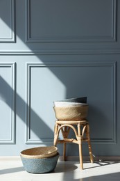 Photo of Stylish stool and many wicker baskets near light grey wall indoors, space for text