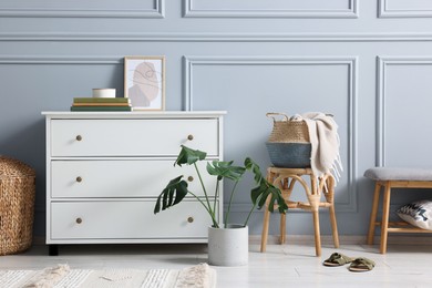 Photo of Stylish interior with stool and chest of drawers near light grey wall