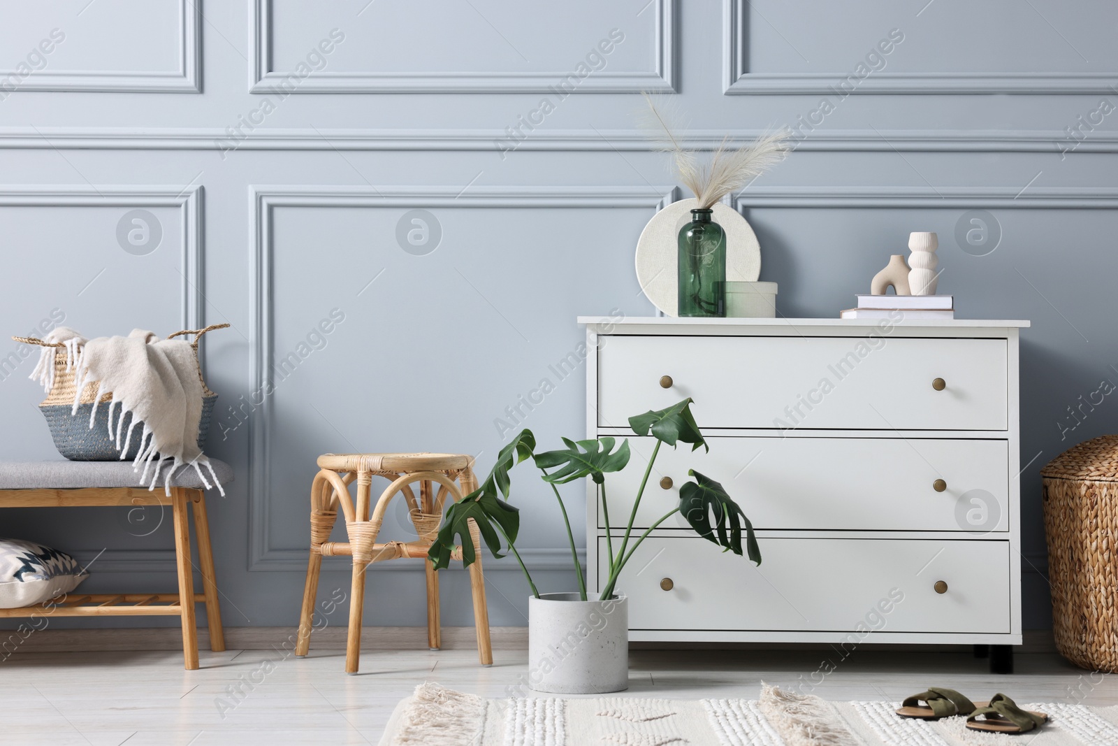 Photo of Stylish interior with stool and chest of drawers near light grey wall