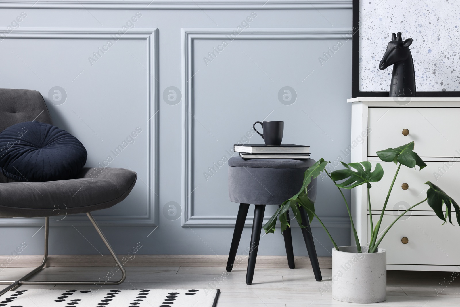 Photo of Stylish interior with stool and chest of drawers near light grey wall