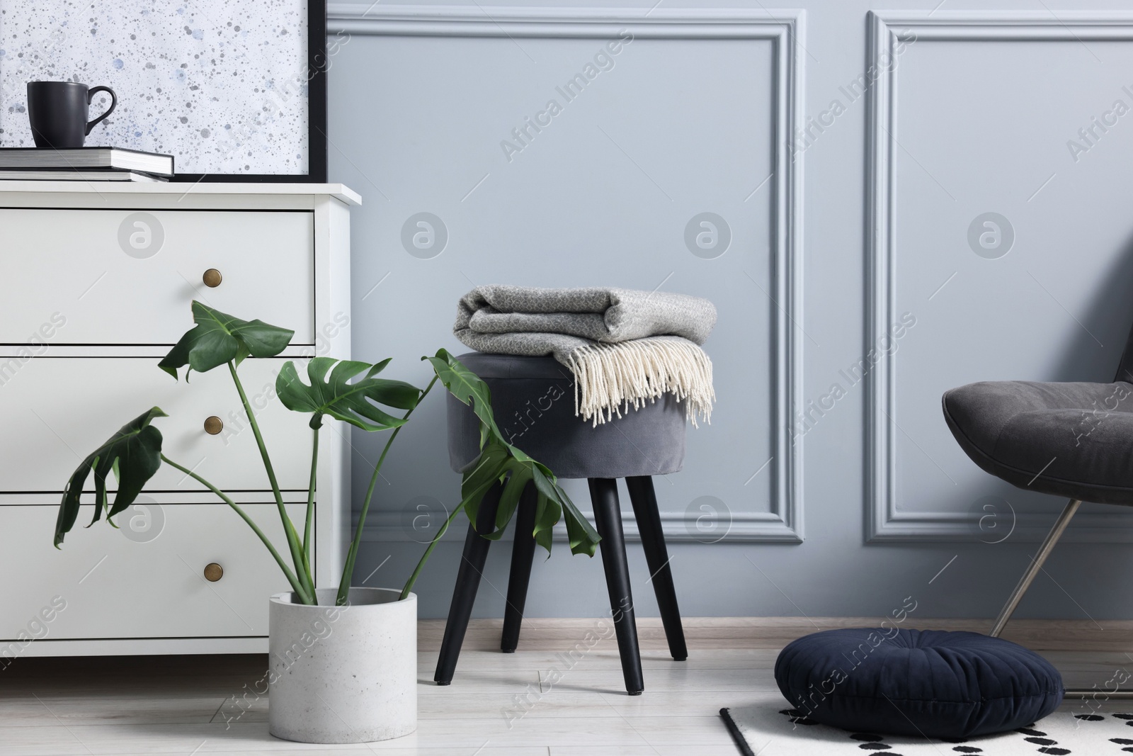 Photo of Stylish interior with stool and chest of drawers near light grey wall