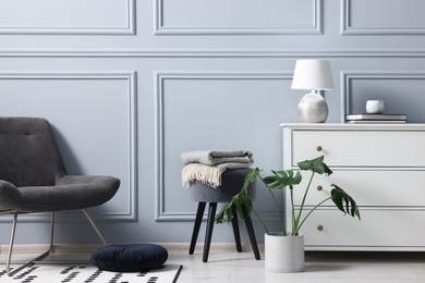 Photo of Stylish interior with stool and chest of drawers near light grey wall