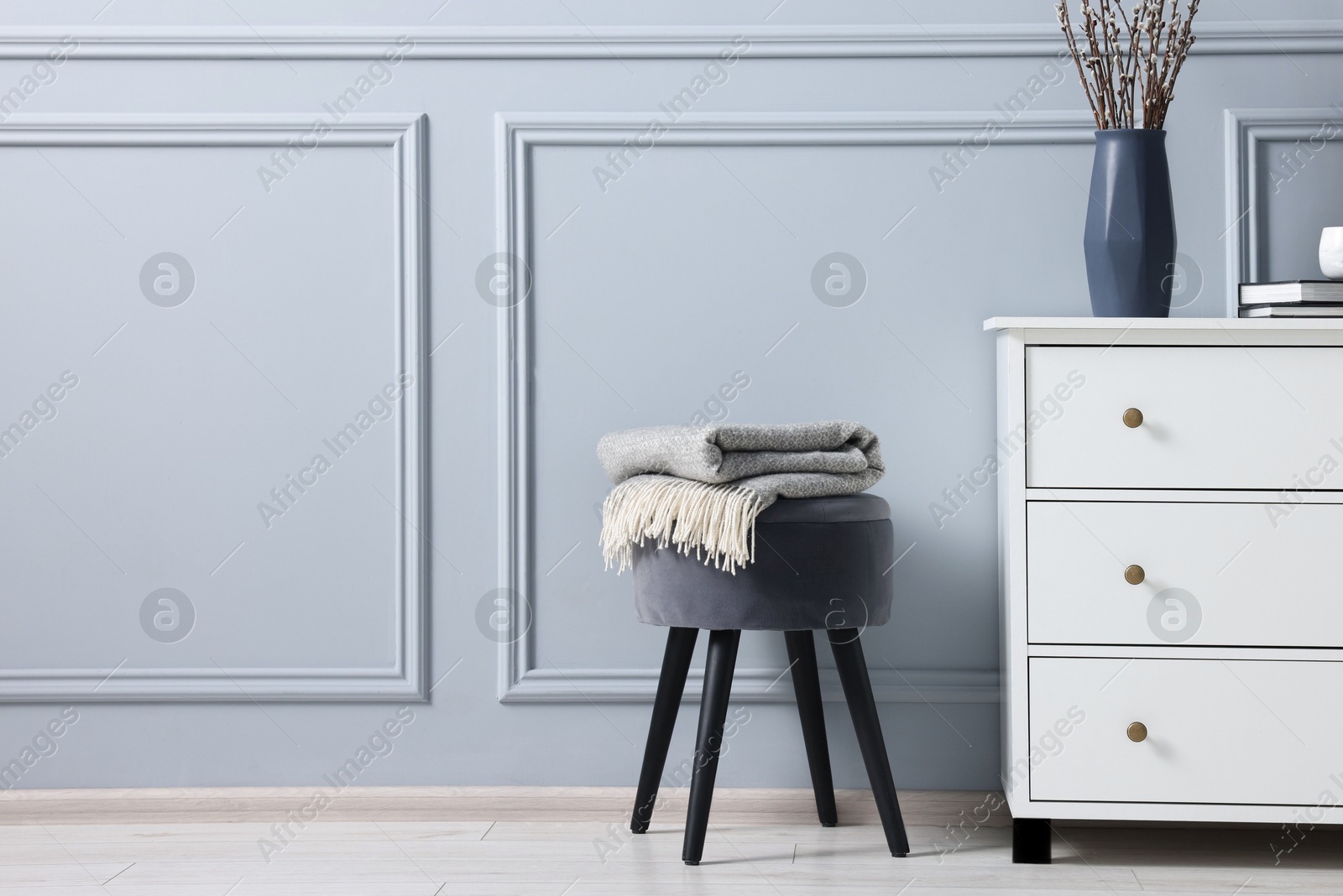 Photo of Stylish interior with stool and chest of drawers near light grey wall, space for text