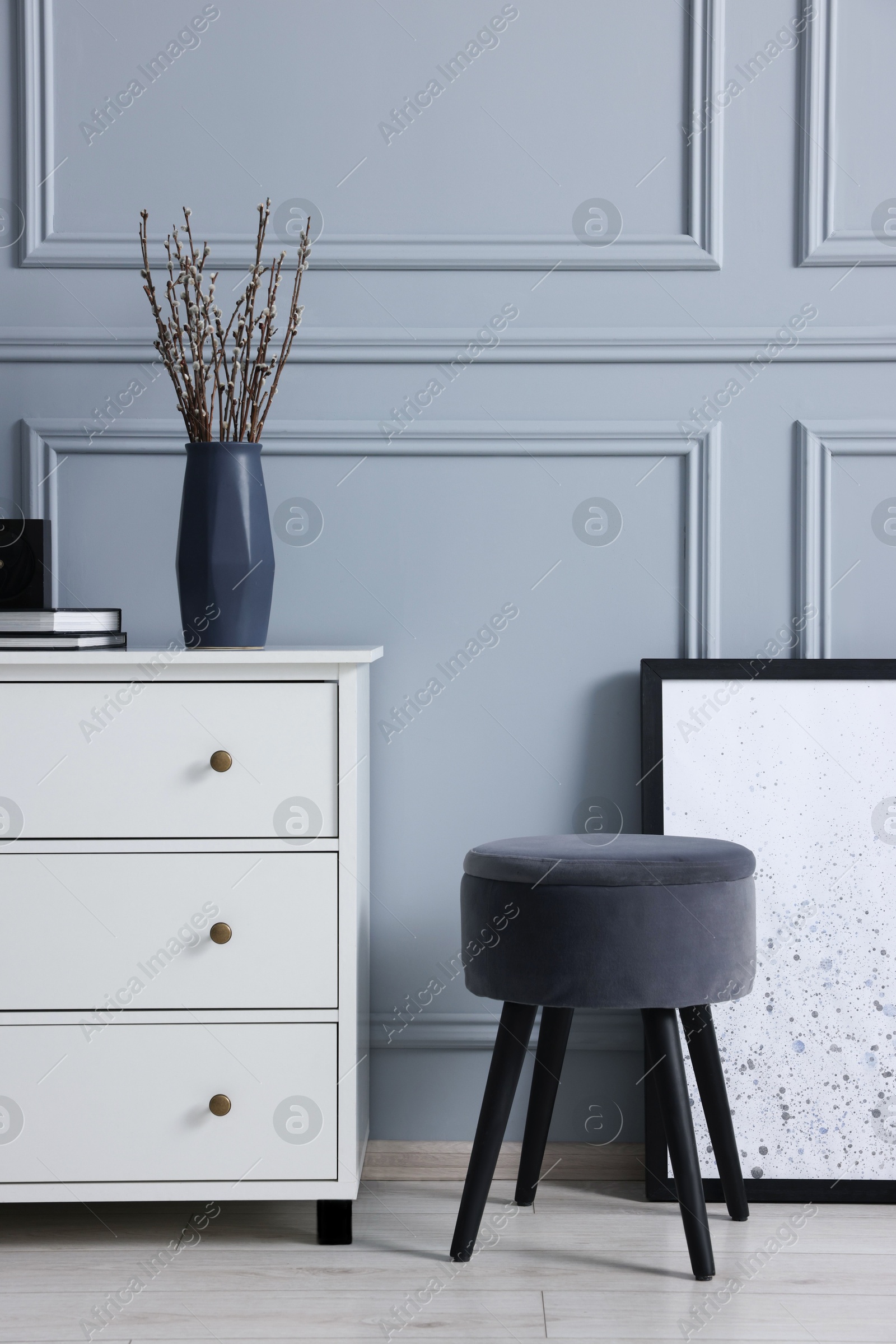 Photo of Stylish interior with stool and chest of drawers near light grey wall