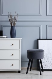 Photo of Stylish interior with stool and chest of drawers near light grey wall