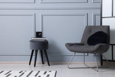 Photo of Stylish stool, chair and books near light grey wall indoors