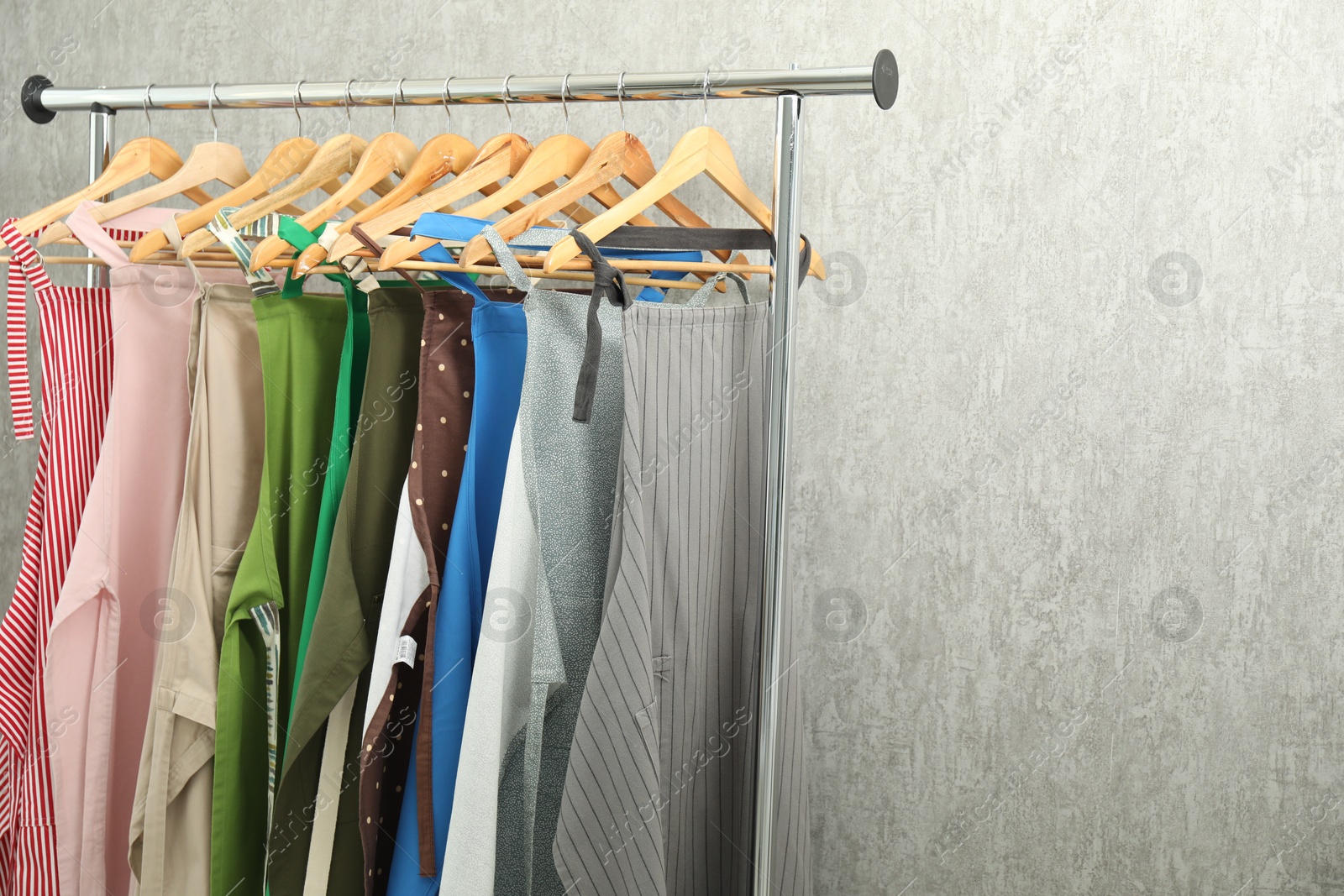 Photo of Many chef's aprons on clothing rack near light grey wall, space for text