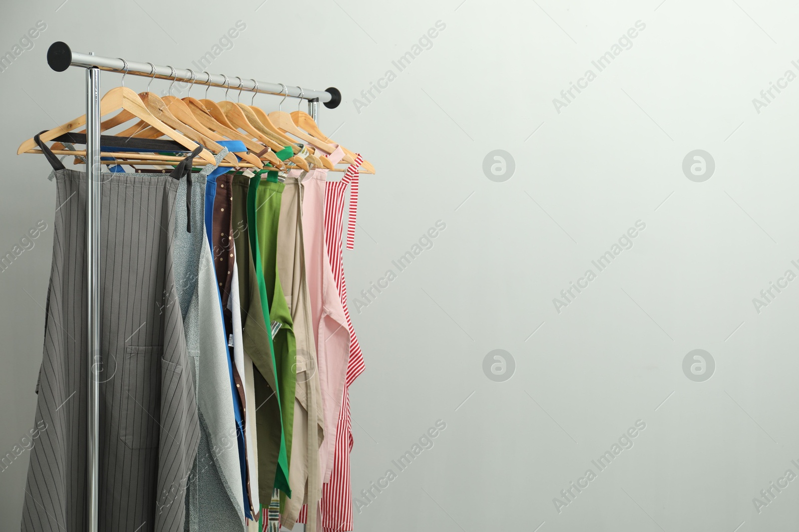 Photo of Many chef's aprons on clothing rack near light grey wall, space for text