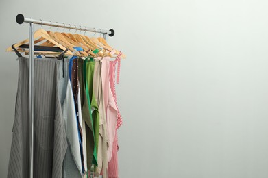 Photo of Many chef's aprons on clothing rack near light grey wall, space for text