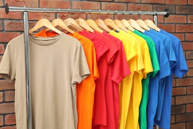 Many colorful t-shirts on clothing rack near brick wall