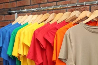 Many colorful t-shirts on clothing rack near brick wall